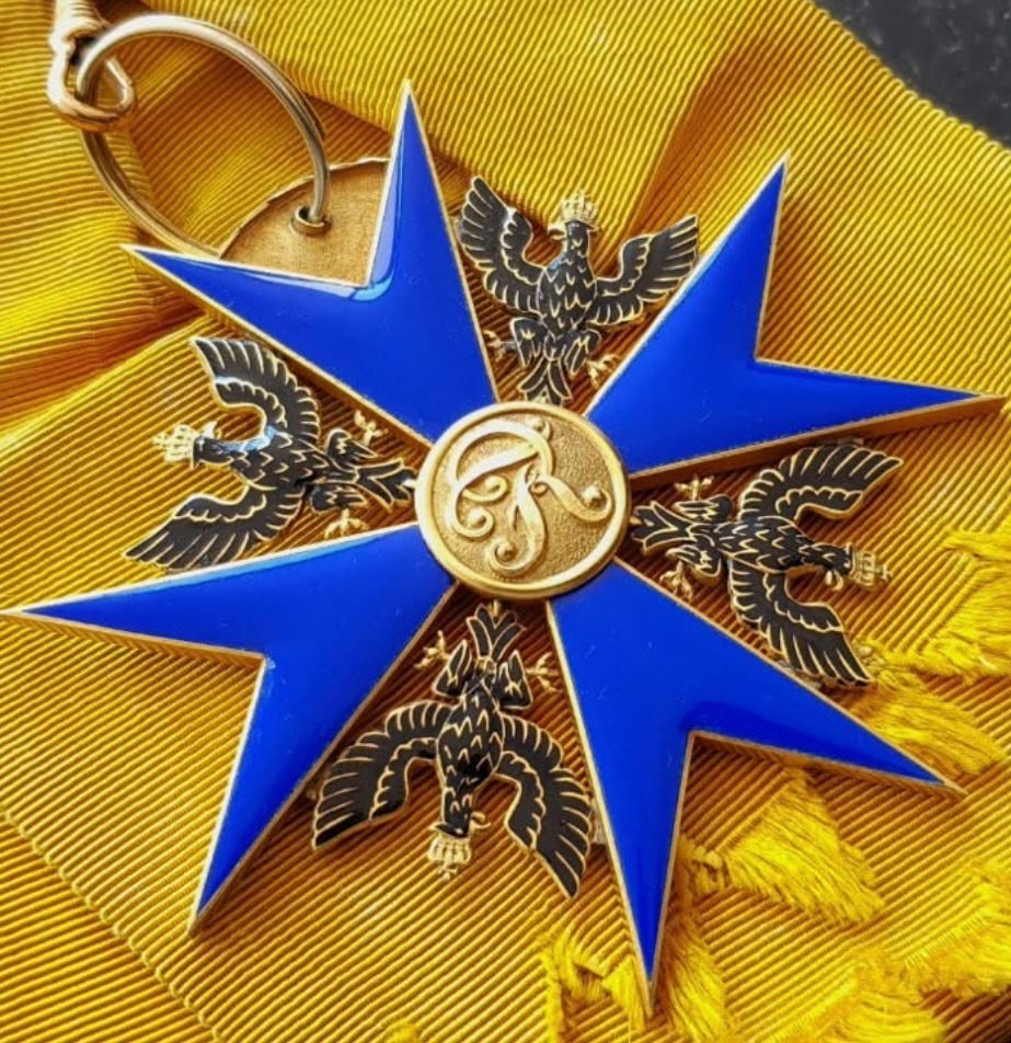 Schwarzer Adlerorden: achtstrahliges Kreuz in blauem Email, vier gekrönte preußische Adler zwischen den Armen und der Namenszug Friedrichs im Medaillon, auf seinem orangefarbenen Band.