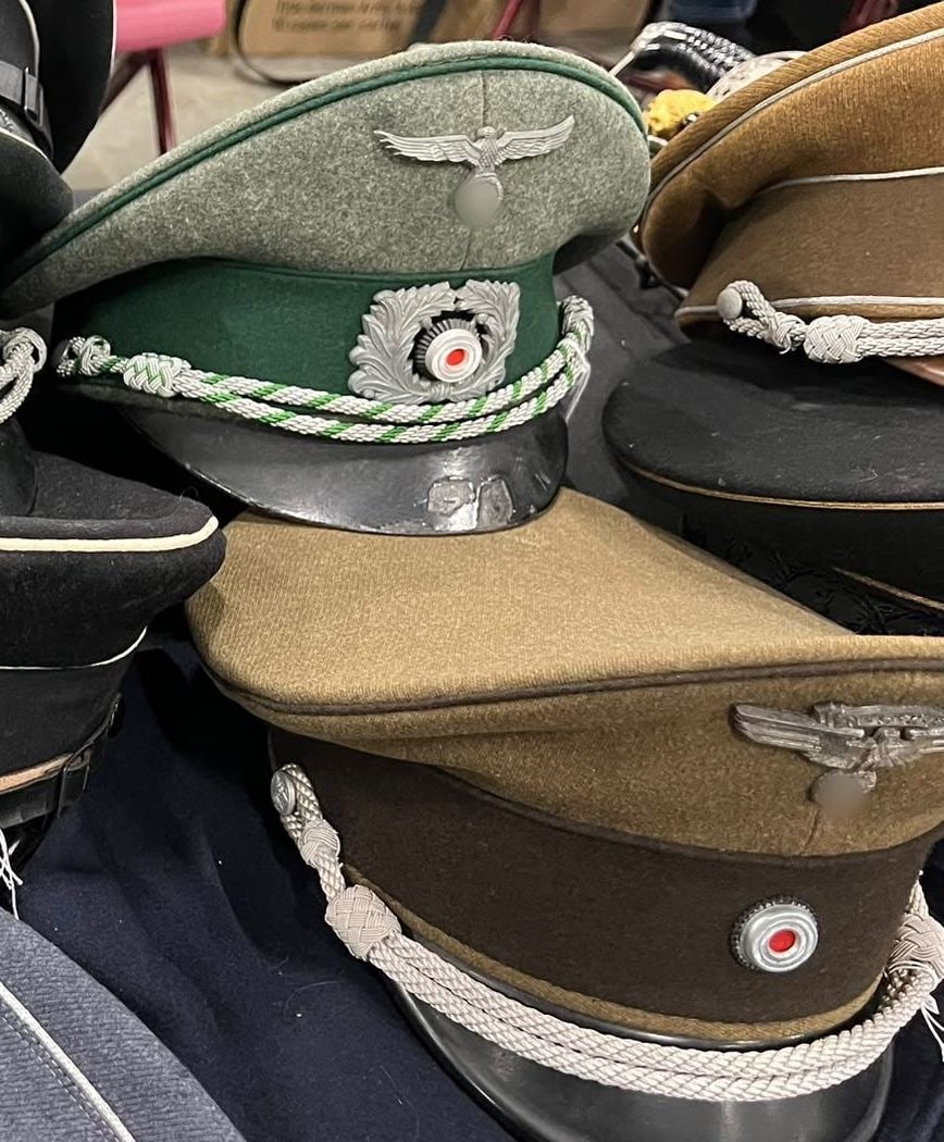 Schirmmützen für Offiziere mit silberner Mützenkordel, Eichenlaubkranz und Kokarde. Die Symbole sind unkenntlich gemacht (§ 86a StGB).