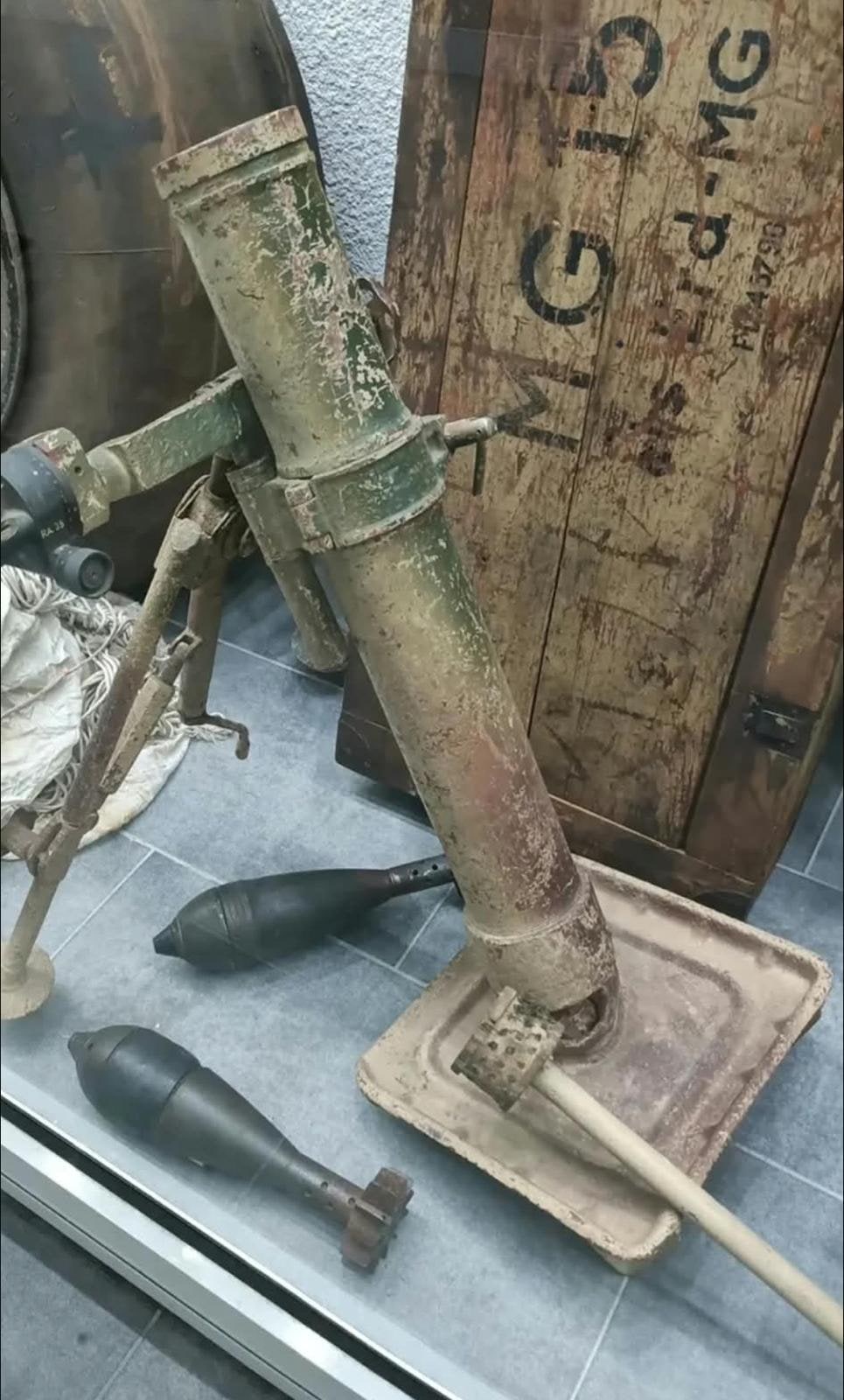 8-cm-Granatwerfer auf Bodenplatte, daneben zwei Wurfgranaten und eine Munitionskiste.