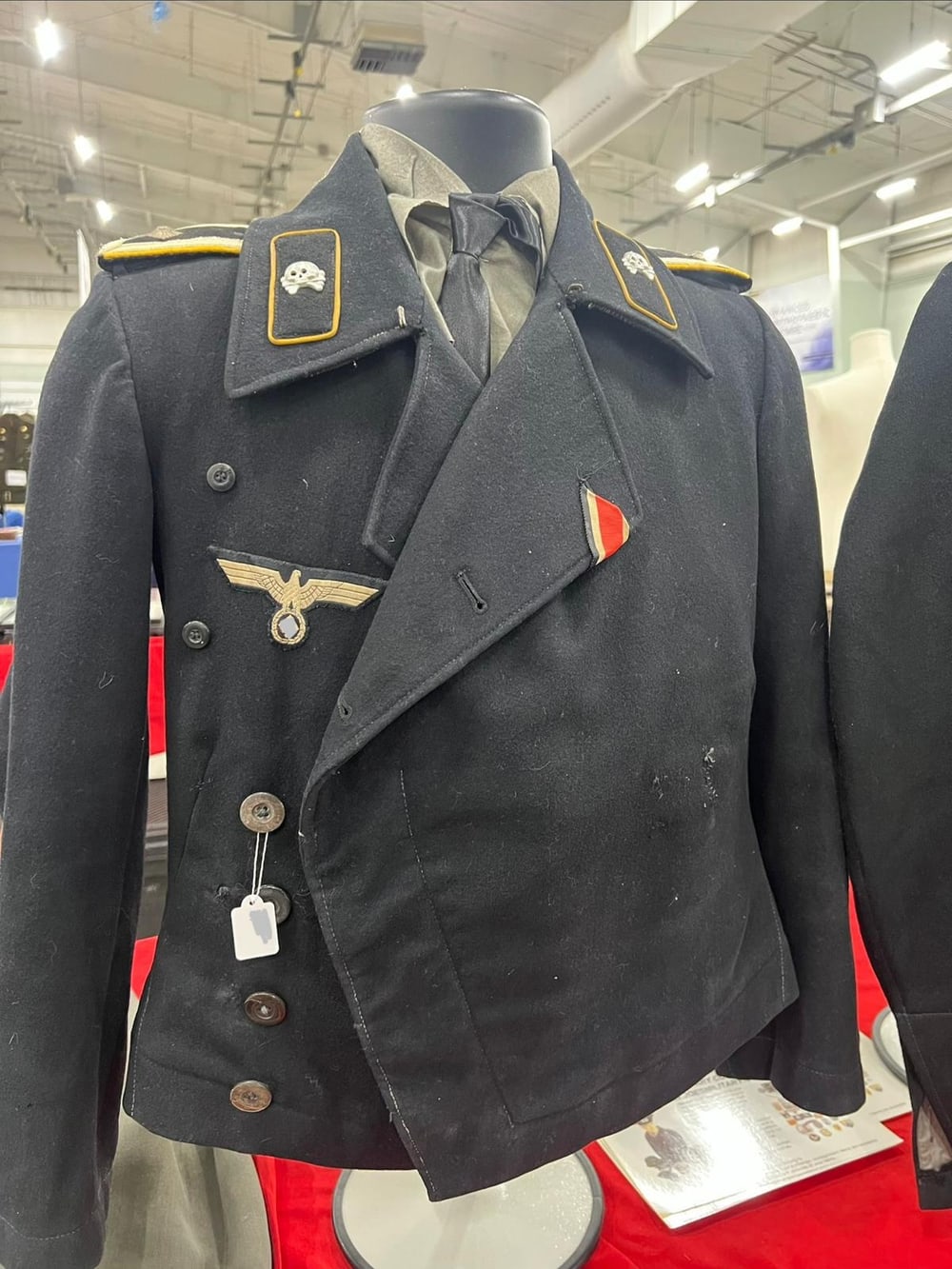 Chaqueta negra de carrista M1938, temprana, de oficial: las calaveras de las tropas acorazadas en el cuello y la cinta de la Cruz de Hierro. El símbolo del águila va tapado (§ 86a StGB).