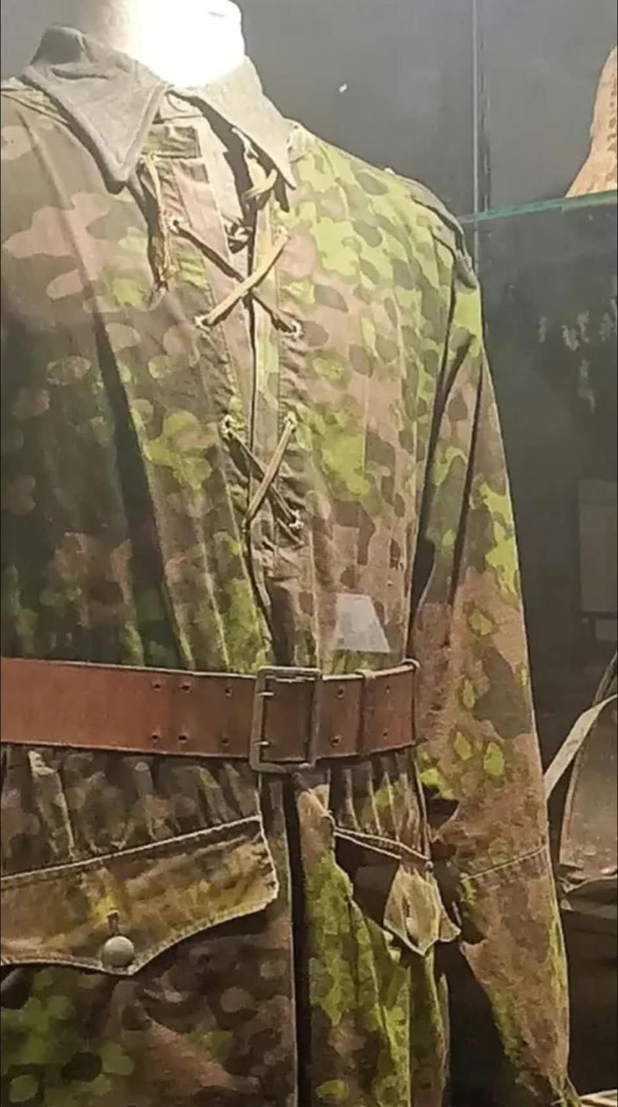 Chaqueta de camuflaje moteado con cordón en el cuello y cinturón de cuero. Usada, no reproducción.