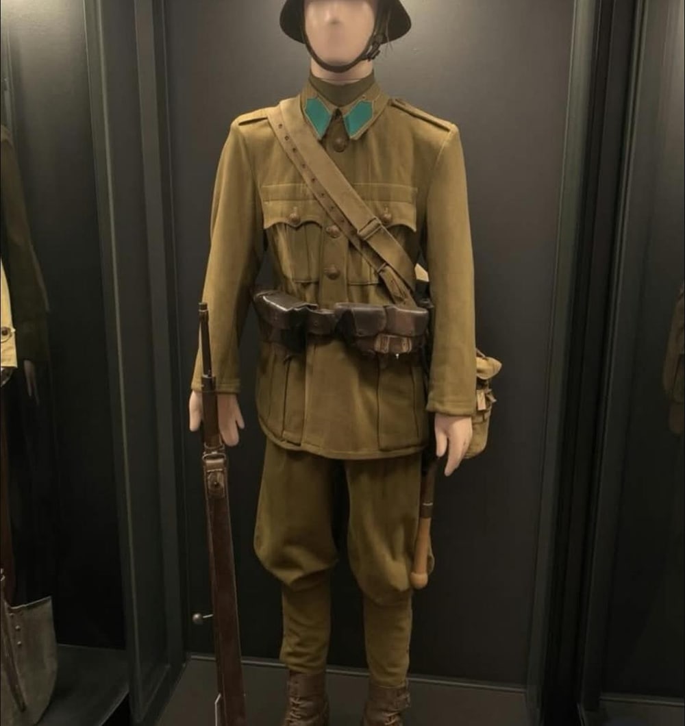 Guerrera caqui con parches de cuello, cartucheras de cuero y polainas de vendaje.
